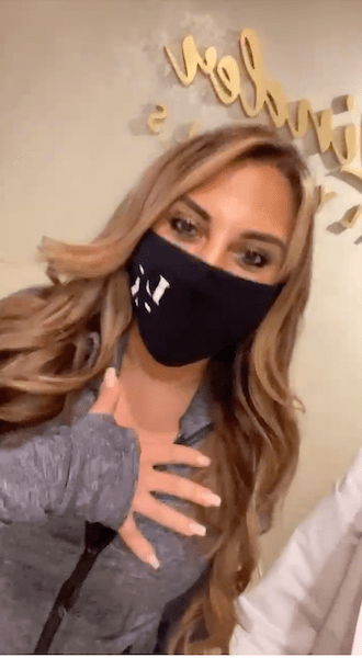 Woman wearing face mask with her hand over her heart.