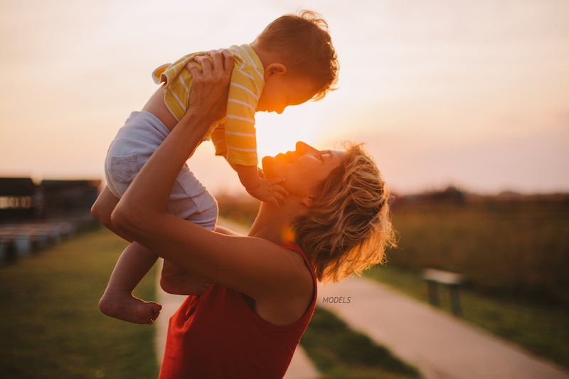 Mother lifting her toddler over her head outdoors.